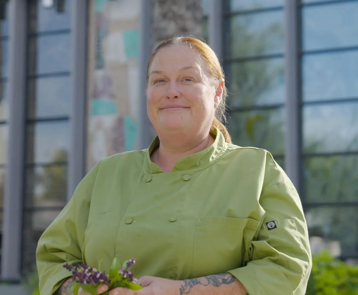 Chef Charleen Badman in a green chef coat holding herbs outdoors, featured in Visit Phoenix’s Sonoran Food Guide story.
