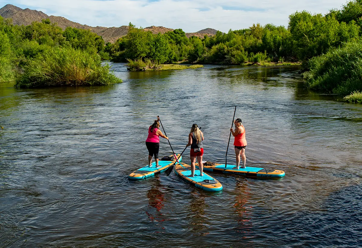 Three paddleboarders floating the Salt River through the Sonoran Desert near Phoenix, Arizona on a sunny spring day.