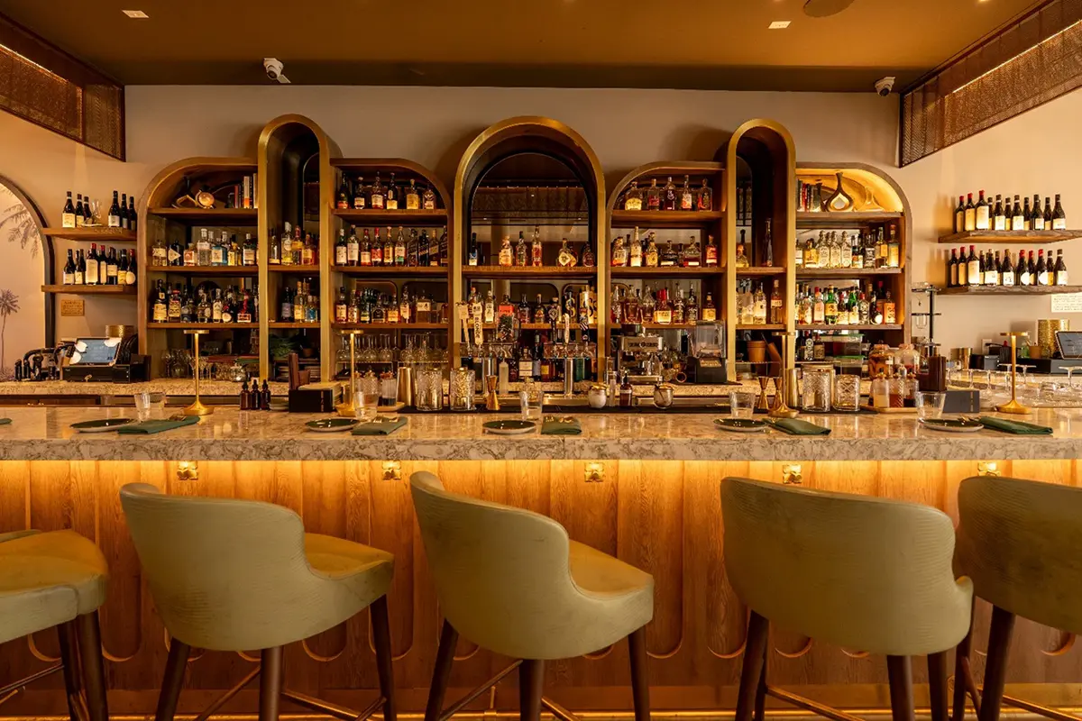 Stylish Phoenix restaurant bar with golden arches, backlit liquor shelves, marble counter, and sage green velvet stools.