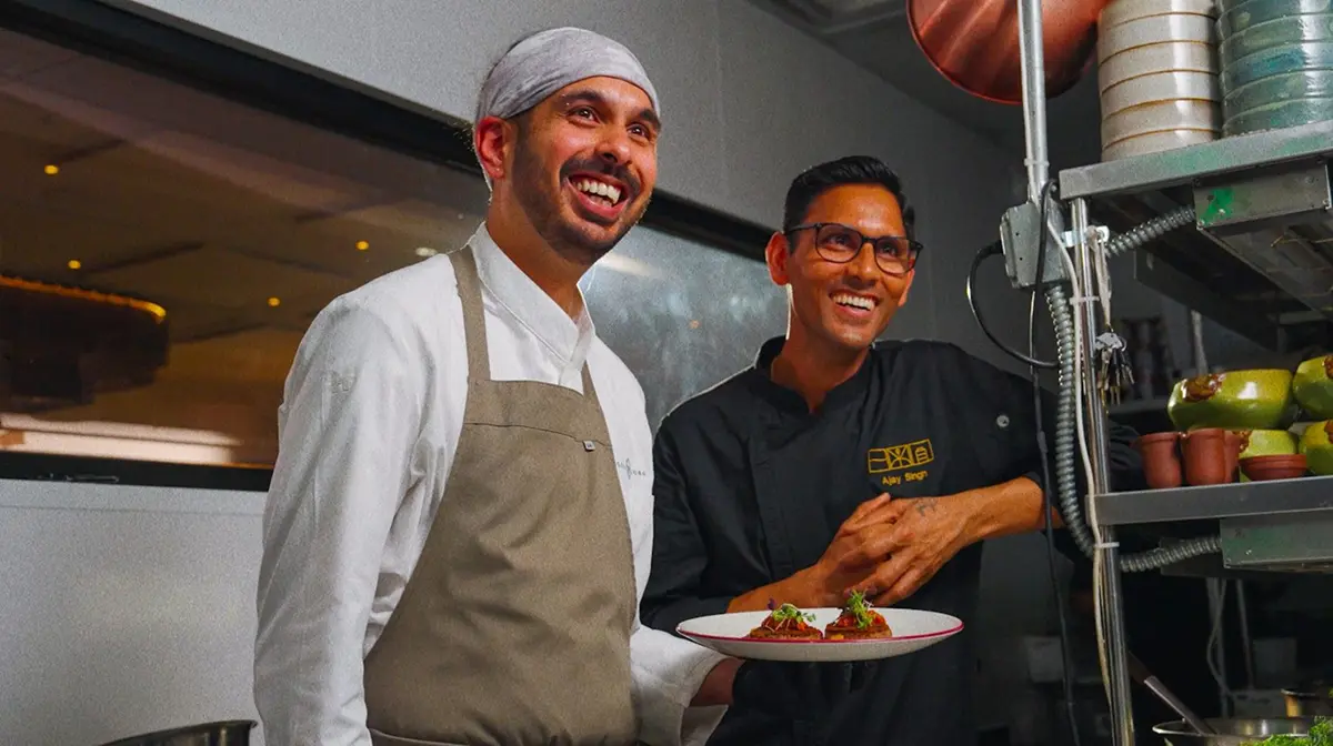 Chef Nigel and Tandoor Master Ajay Singh smiling in the Indibar kitchen while plating a tepary bean dish.